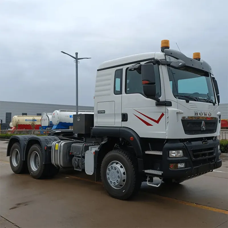 HOWO TX tractor truck pulling a low-bed trailer with heavy equipment on a laterite road
